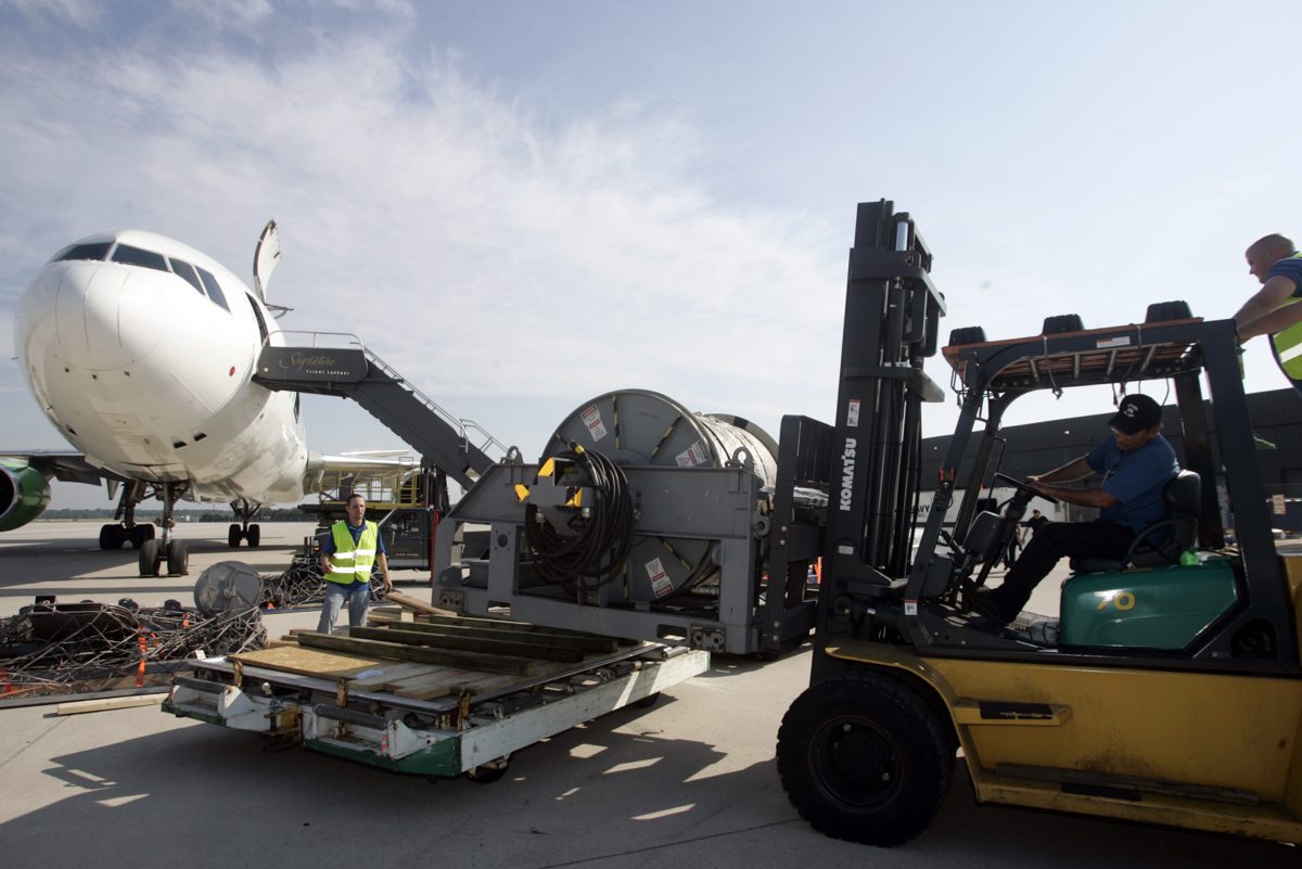 Ground crew loading freight onto a pallet beside a commercial airliner at the airport cargo terminal